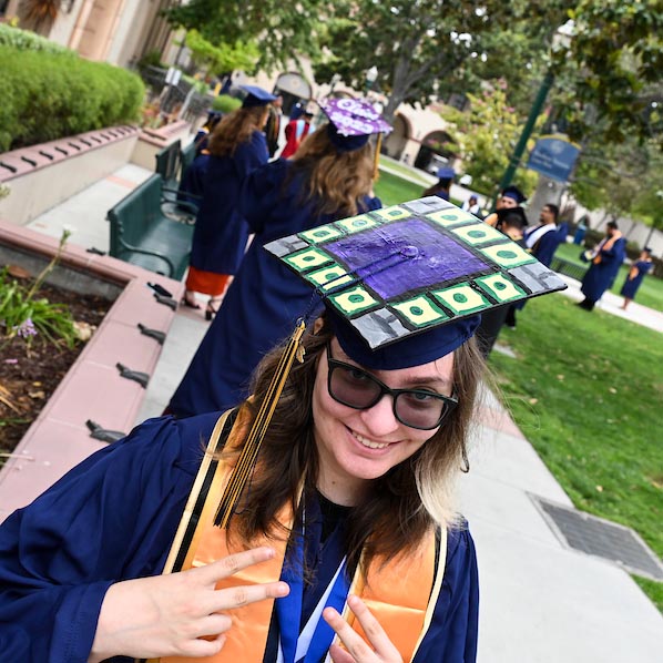 A Fullerton College student in regalia gives a peace sign to the camera during graduation.