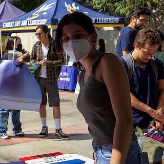 A Fullerton College student in a mask looks into the camera at a campus event.